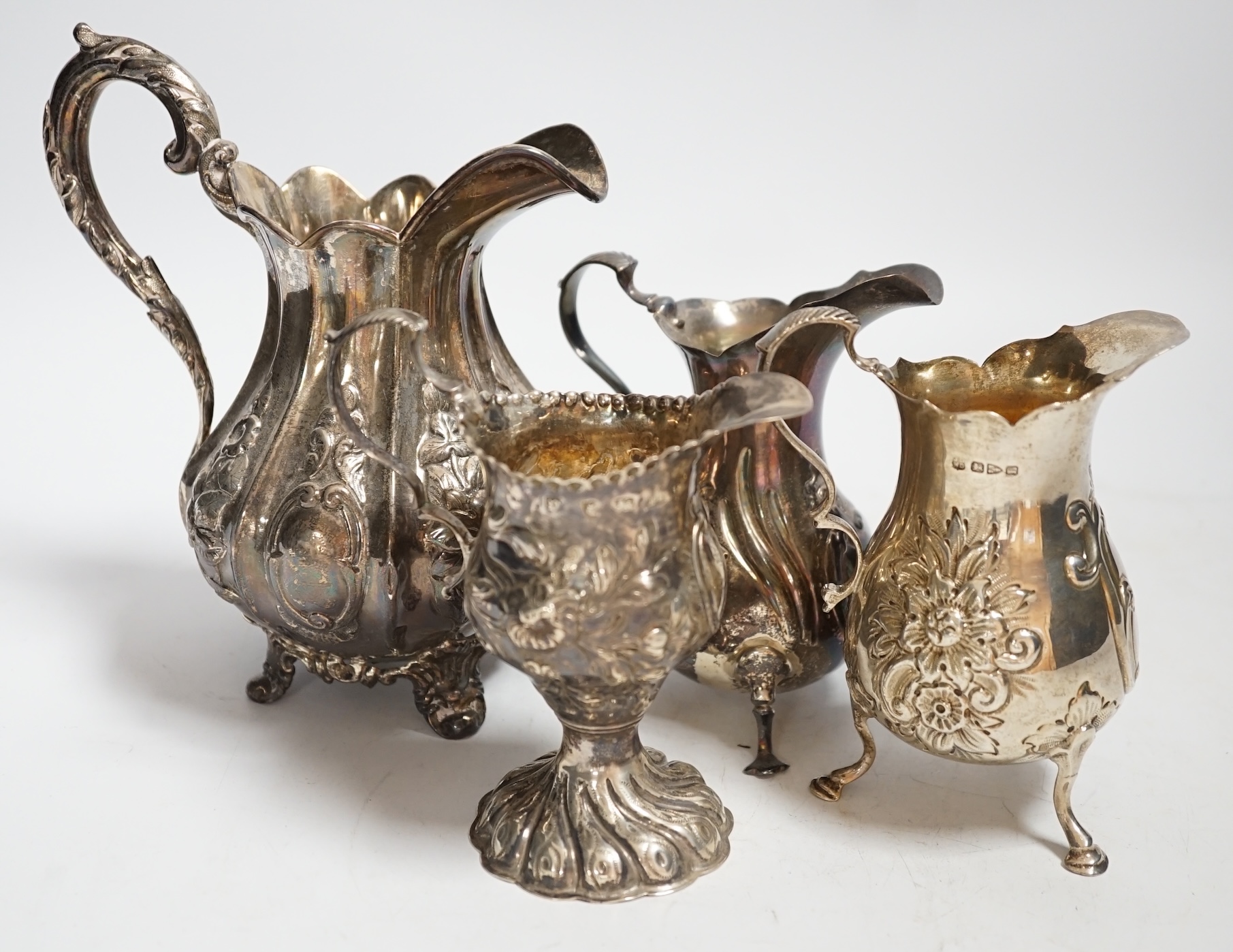 A George III inverts pear shaped cream jug with later embossed decoration, 11.2cm and three later silver cream jugs including two Victorian, 17.4oz.